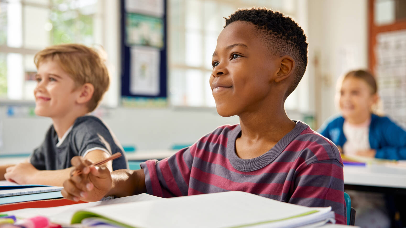Two kids in class sitting at desk with school supplies