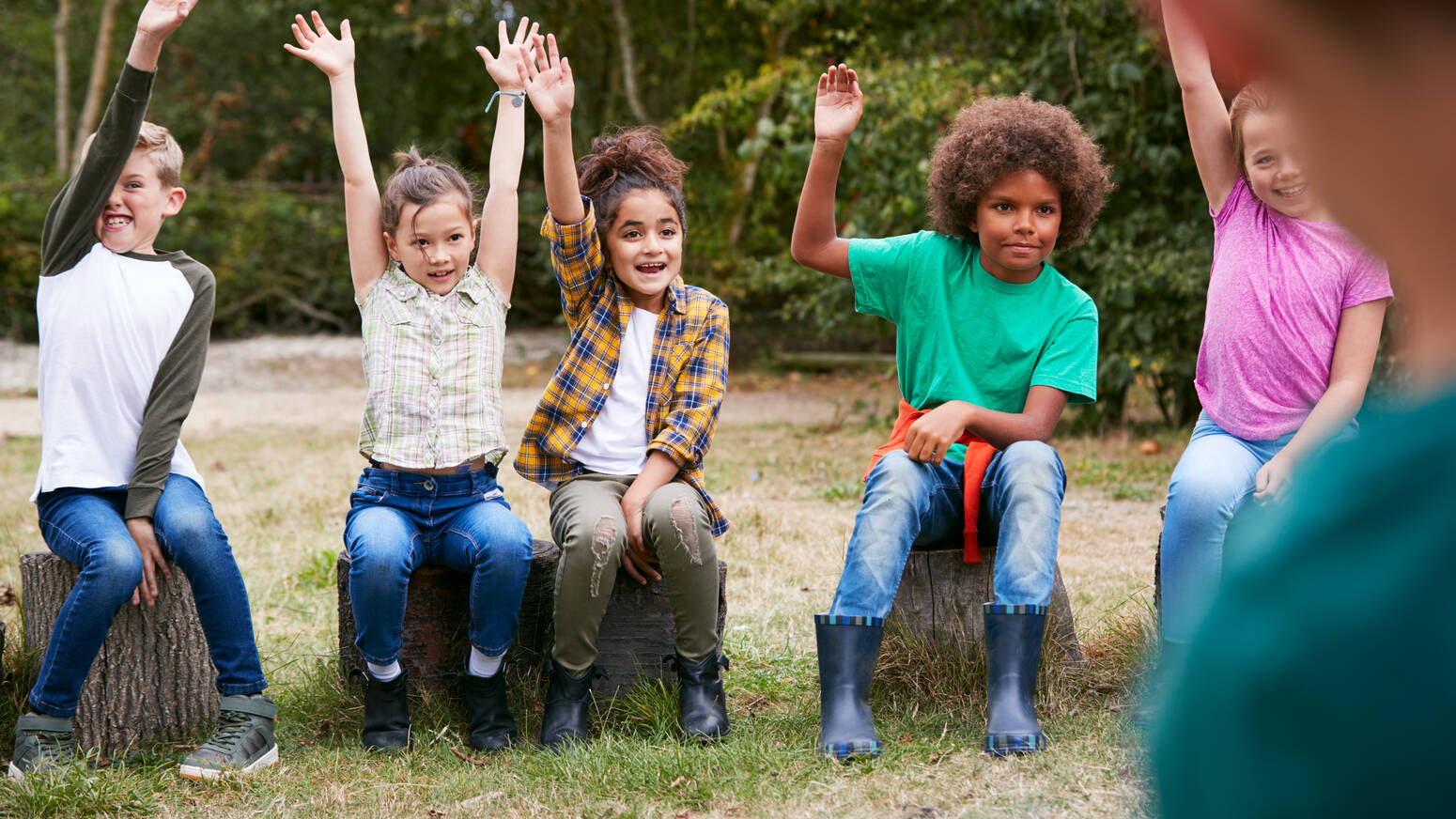 Group of kids sitting outside raising their hands
