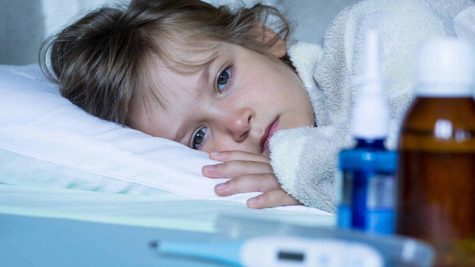 sick child laying in bed looking at thermometer