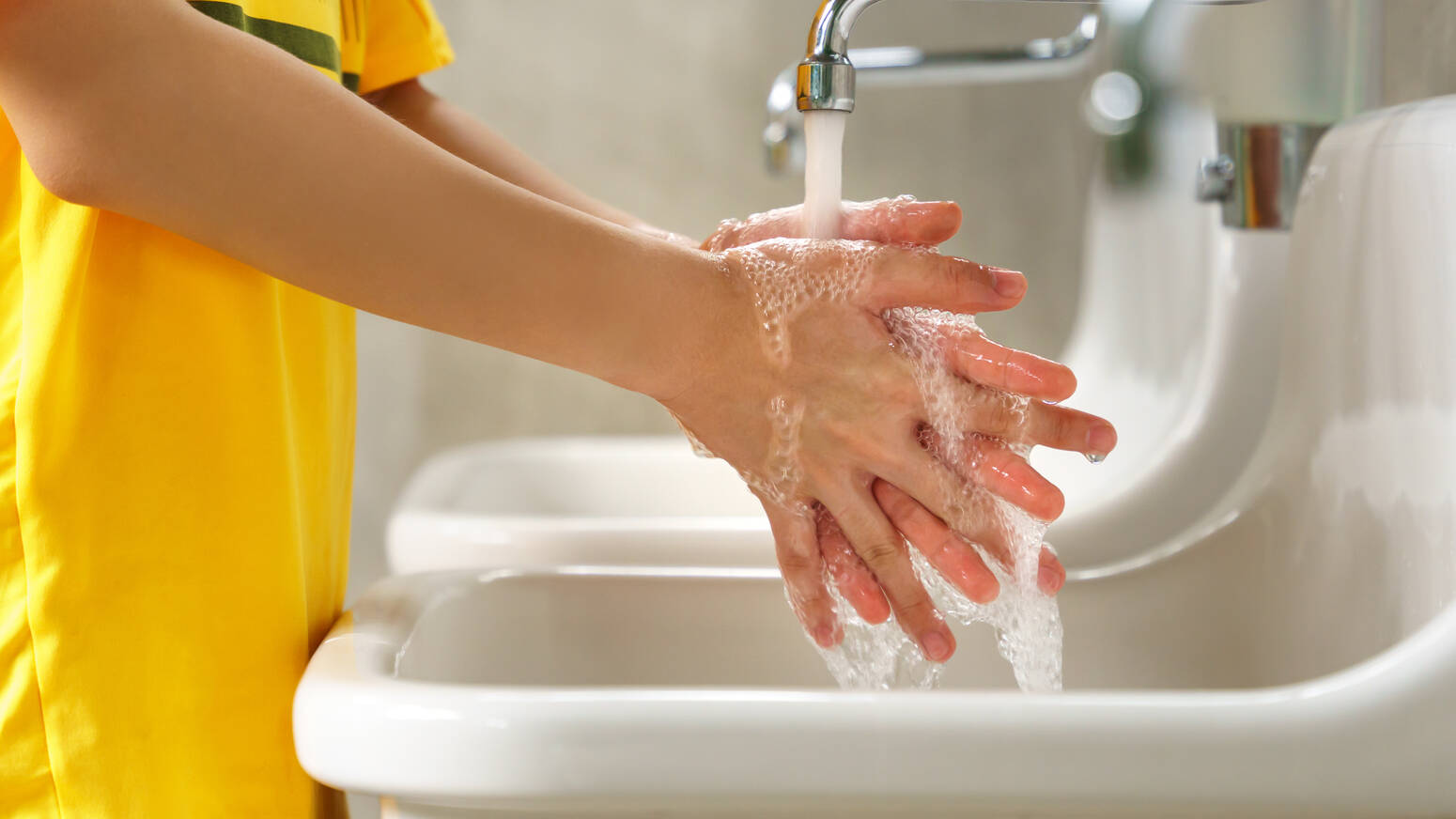 child in yellow shirt washing hands