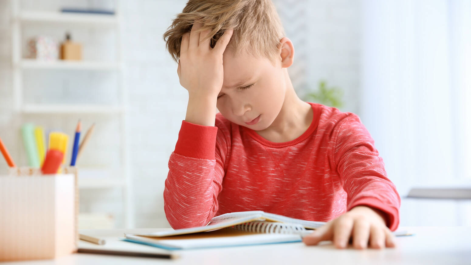 boy sitting at table in pain holding his head