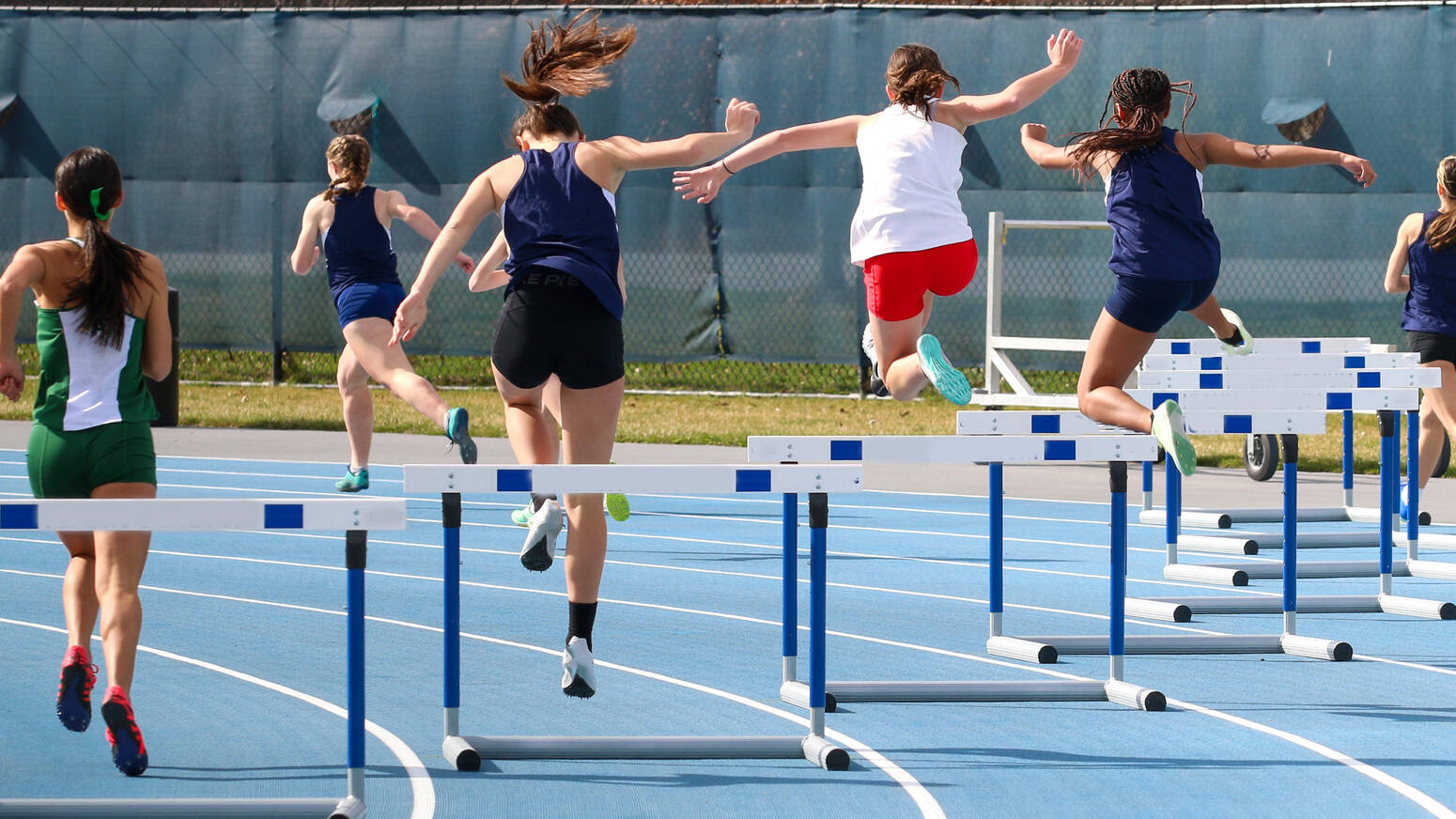 teen runners jumping hurdles on track