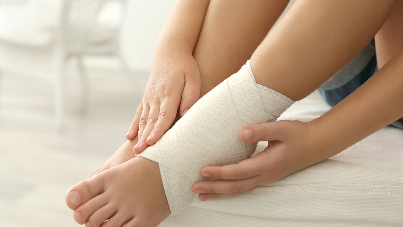 child sitting with injured ankle that is wrapped with bandage