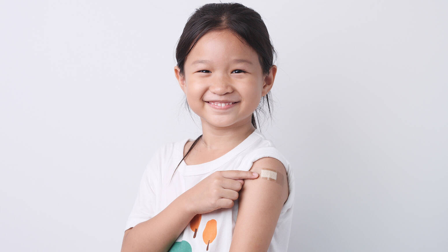 girl smiling pointing to band aid on arm