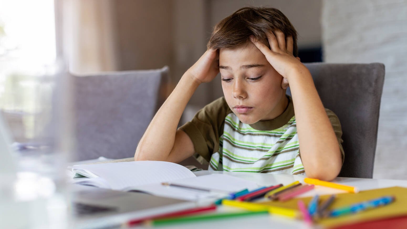 Kid sitting at table hands over head stressed looking at homework