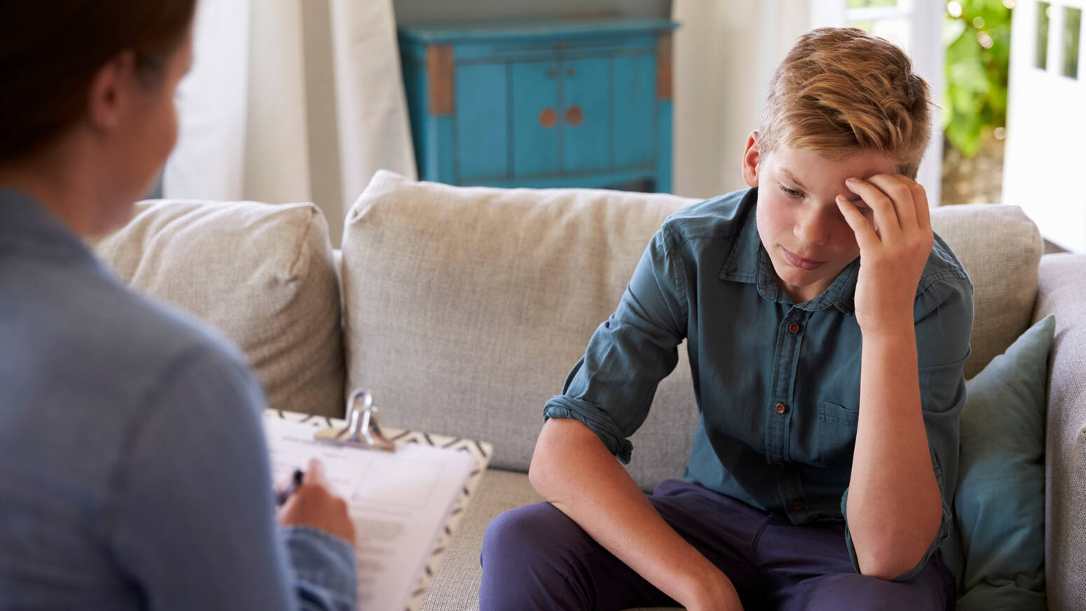 Adult talking to kid on couch holding a clipboard