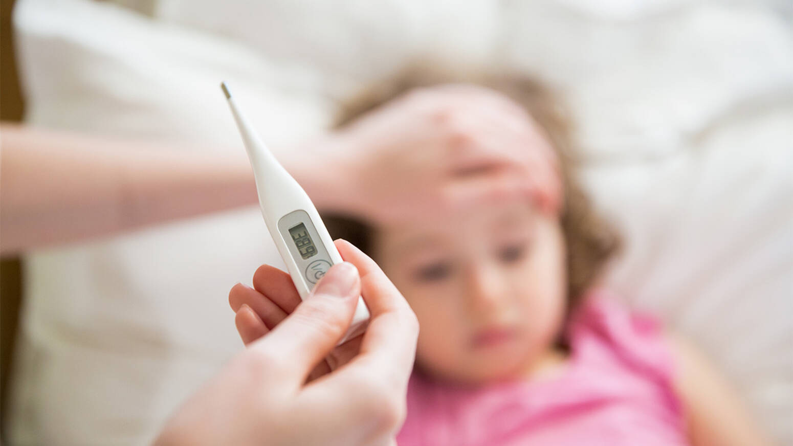 Caregiver reading thermometer with other hand on child's forehead.