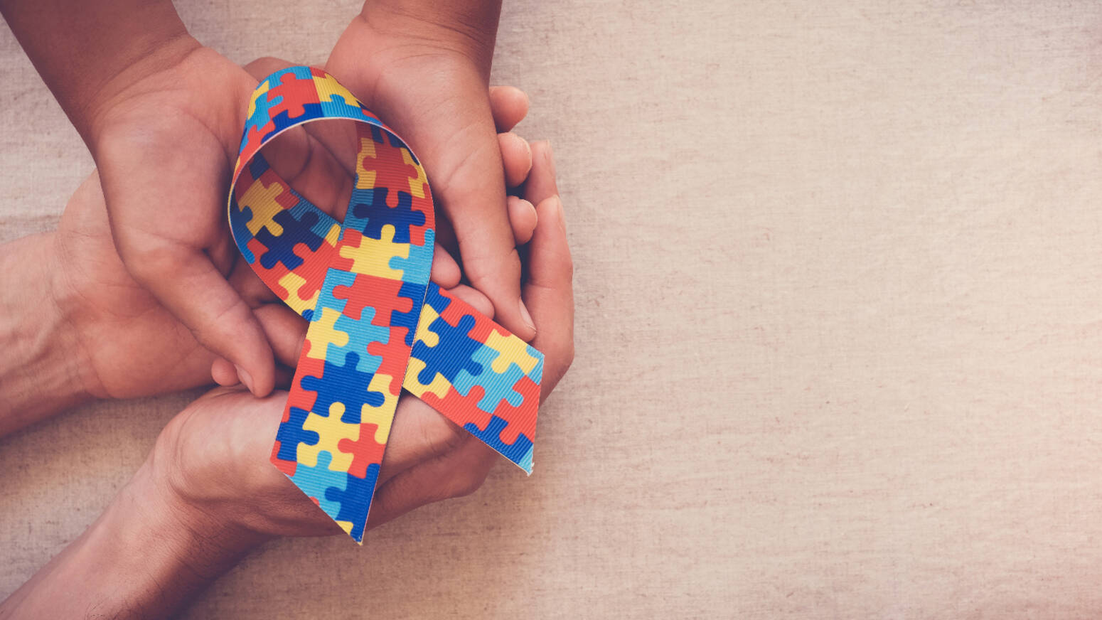 Image of adult and child hands hold a puzzle-piece printed autism ribbon
