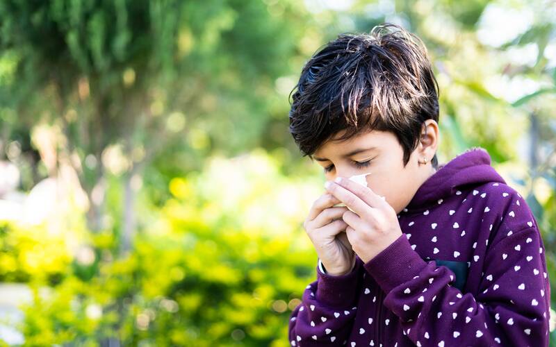boy wearing purple sweatshirt blowing nose