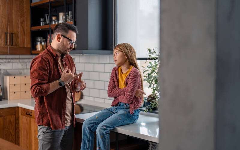 Child sitting on kitchen counter while parent talks to them