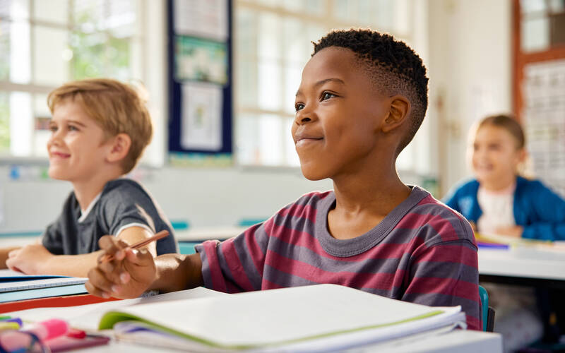 Two kids in class sitting at desk with school supplies