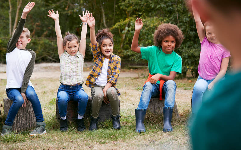 Group of kids sitting outside raising their hands
