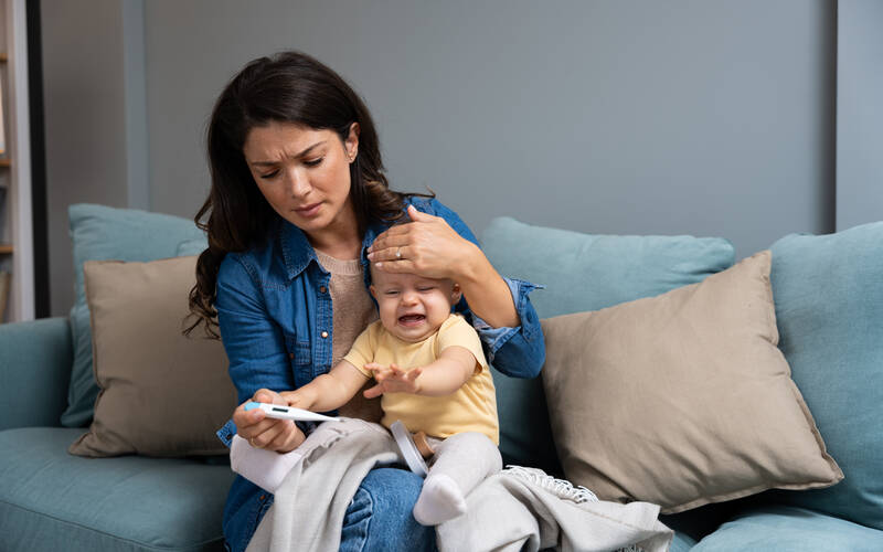mom checking thermometer and comforting sick child