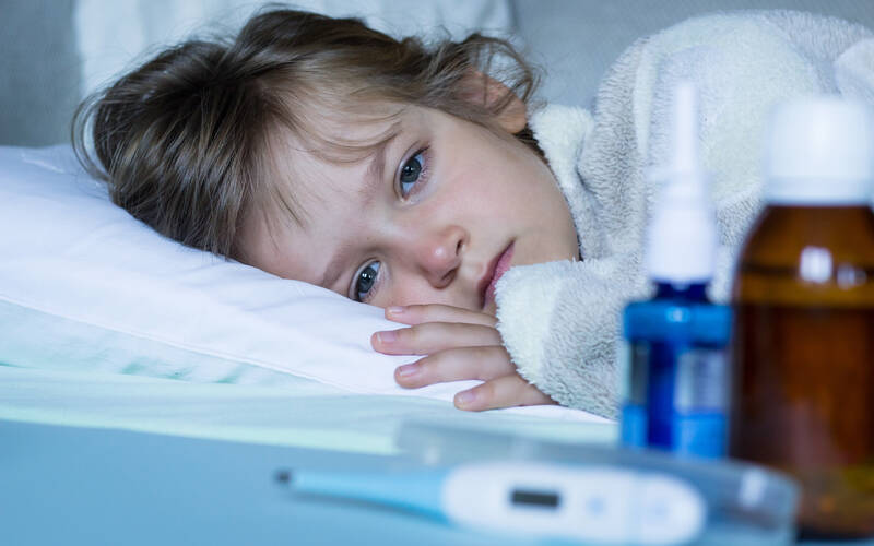 sick child laying in bed looking at thermometer
