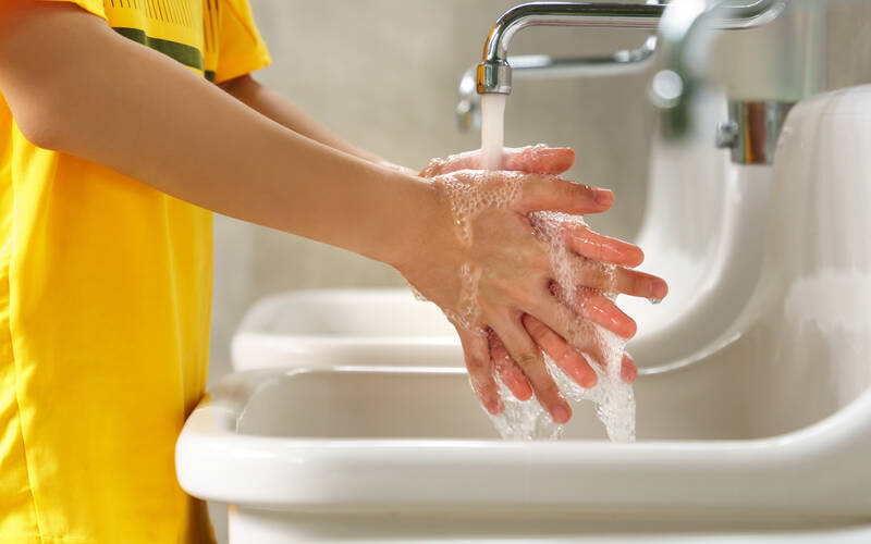 child in yellow shirt washing hands