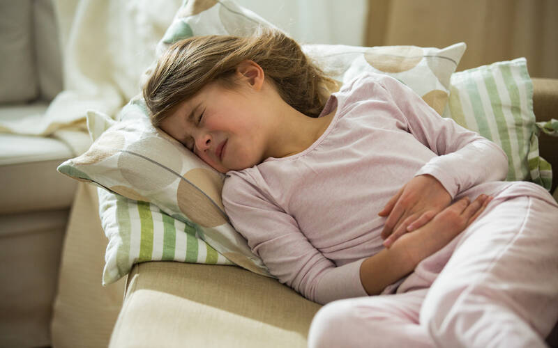 young girl on couch holding her stomach 