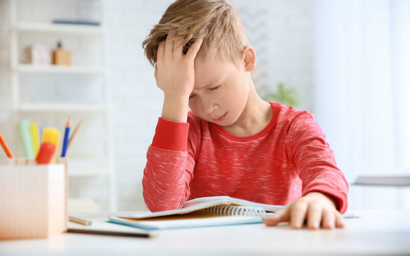 boy sitting at table in pain holding his head