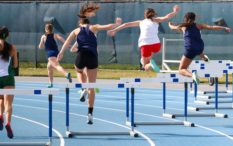 teen runners jumping hurdles on track