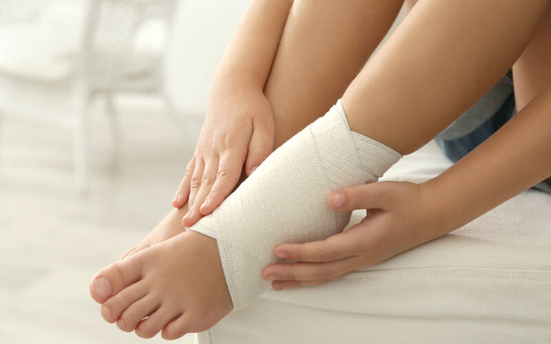 child sitting with injured ankle that is wrapped with bandage