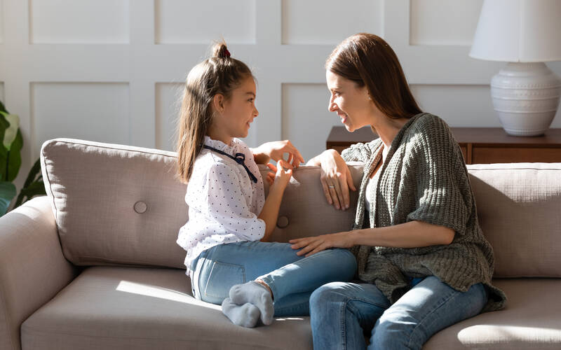 Young child and adult sit on couch talking