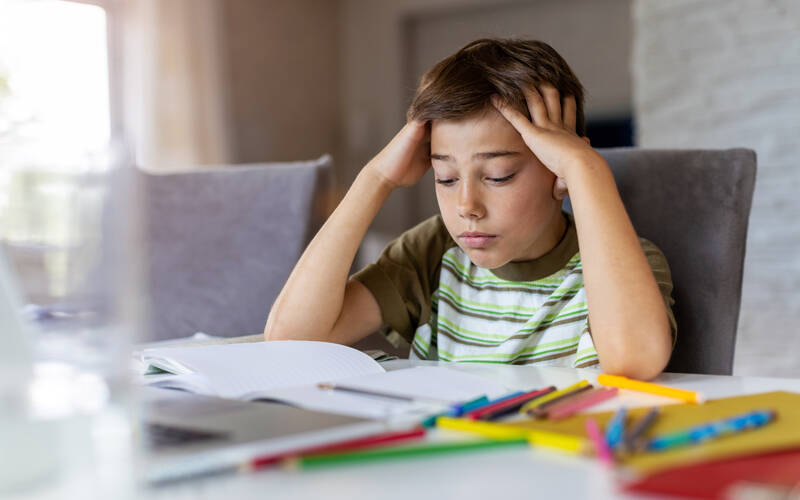 Kid sitting at table hands over head stressed looking at homework