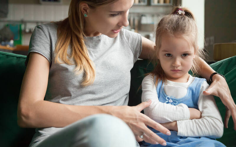 Young child sitting arms crossed with mom trying to comfort