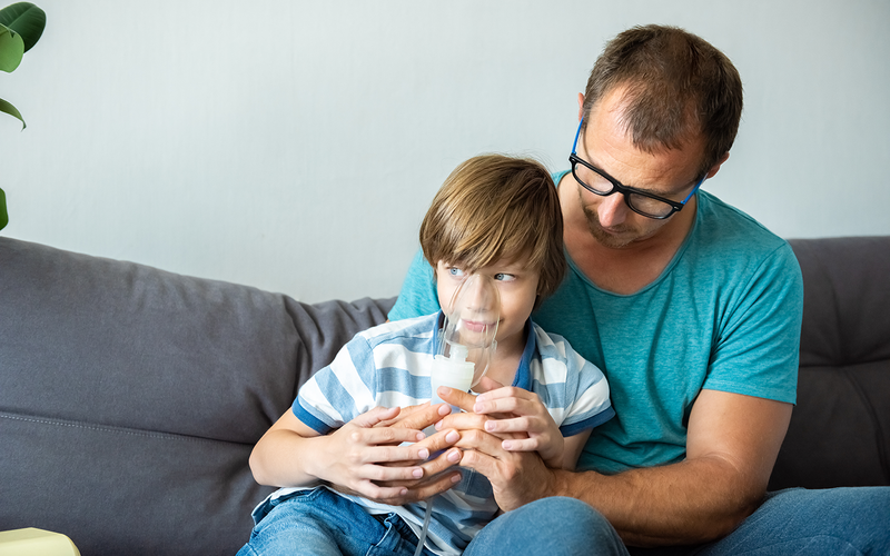 Child using nebulizer in father's nap
