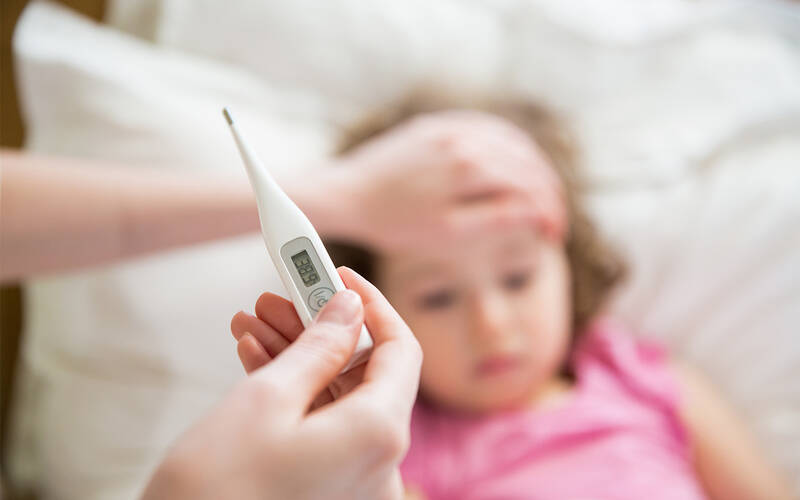 Caregiver reading thermometer with other hand on child's forehead.