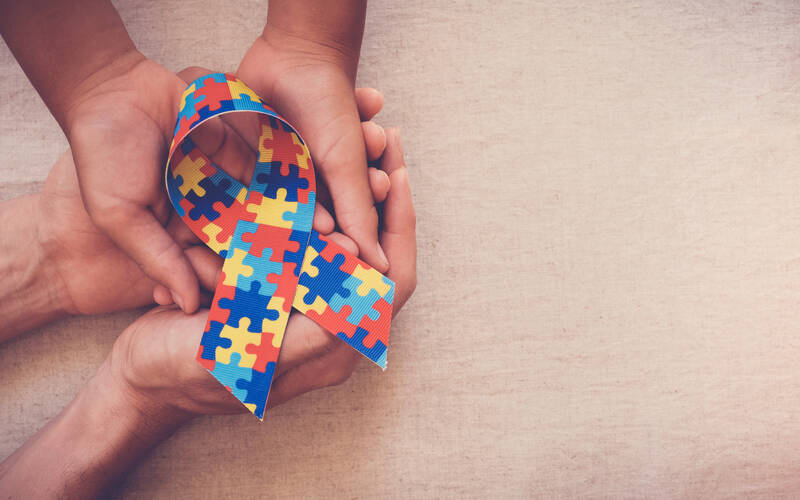 Image of adult and child hands hold a puzzle-piece printed autism ribbon