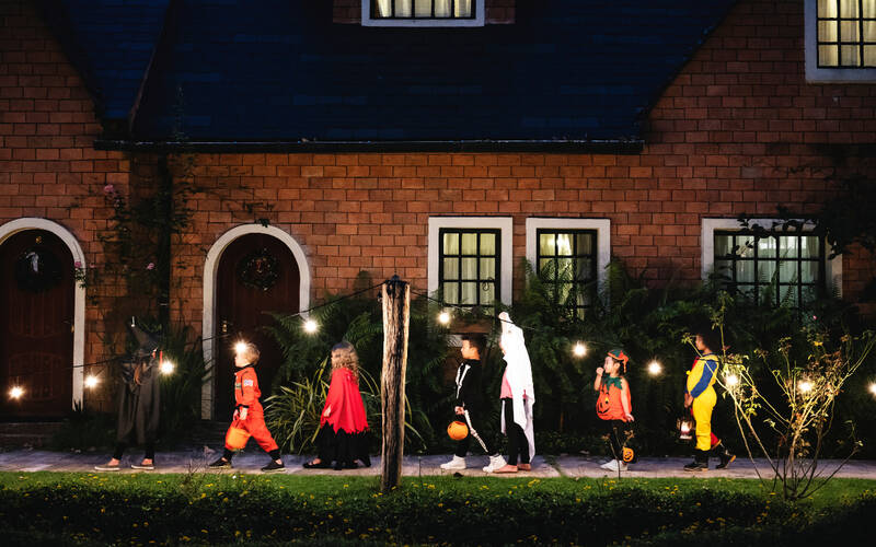 Halloween trick or treaters walking on a sidewalk in a neighborhood at night time.