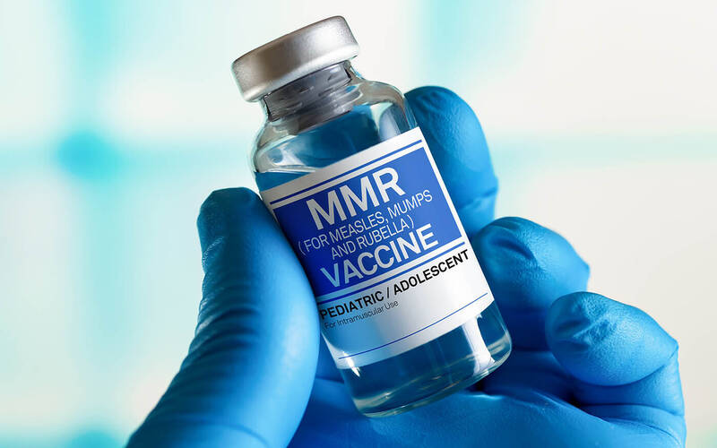 Gloved hand holding MMR vaccine vial.