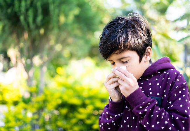boy wearing purple sweatshirt blowing nose