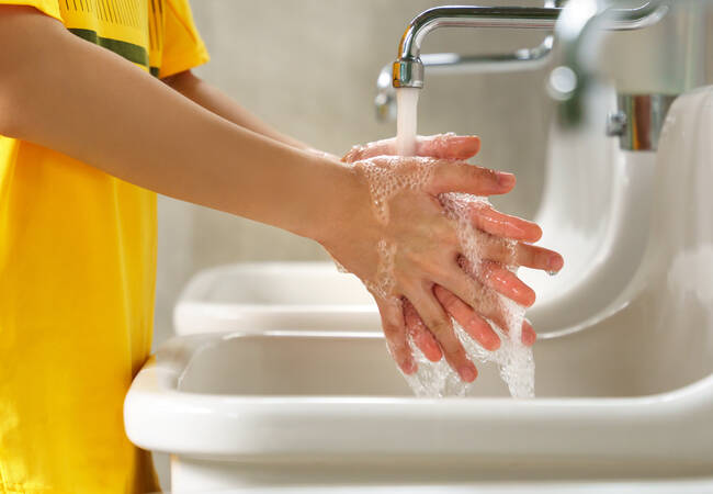 child in yellow shirt washing hands