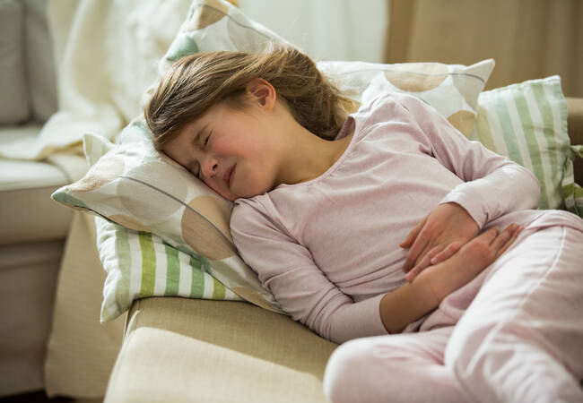young girl on couch holding her stomach 