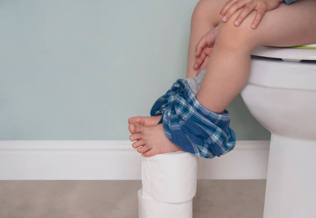 child sitting on toilet with feet on toilet paper rolls