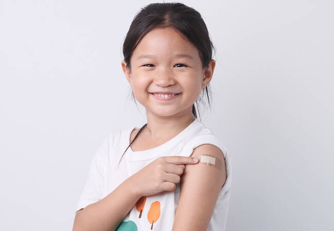 girl smiling pointing to band aid on arm