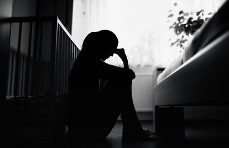 Silhouette photo of woman sitting on ground next to baby crib with her head in her hands