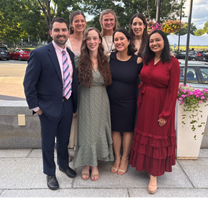 Seven well-dressed people pose for a photograph outside