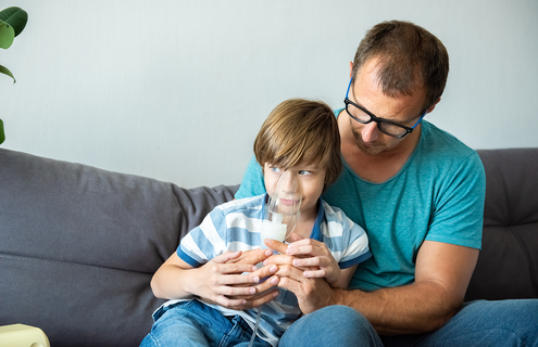 Child using nebulizer in father's nap
