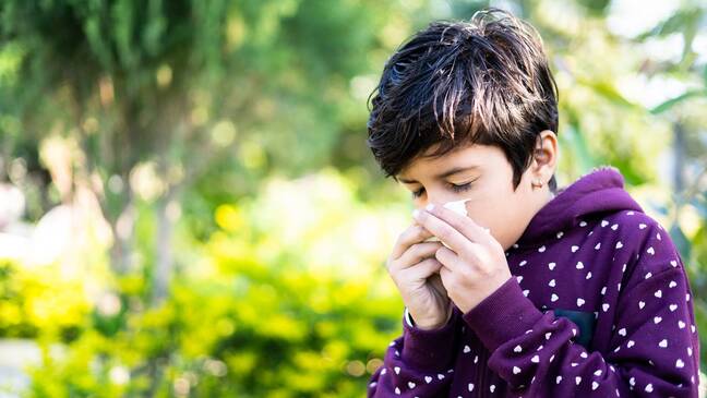 Kid outside blowing nose into tissue