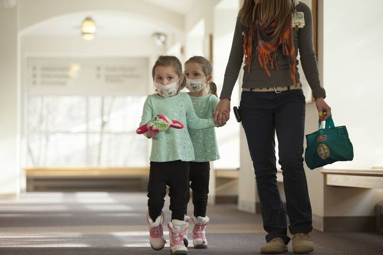 Child life staff member with two young girls in matching clothes wearing medical masks